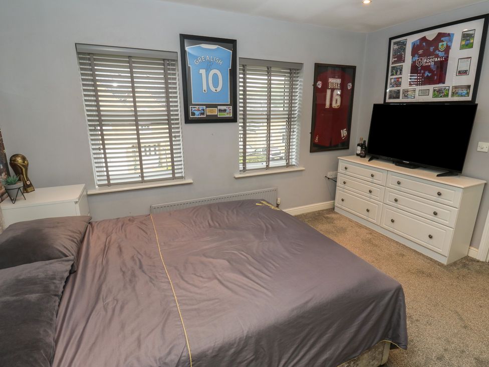 A bedroom with a bed, television, and framed shirts at 20 Overland Crescent in Apperley Bridge