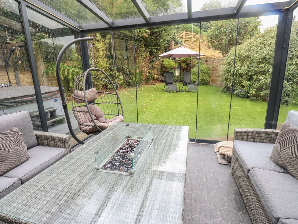 A conservatory with a glass table and hanging chair at Corriegale in Apperley Bridge