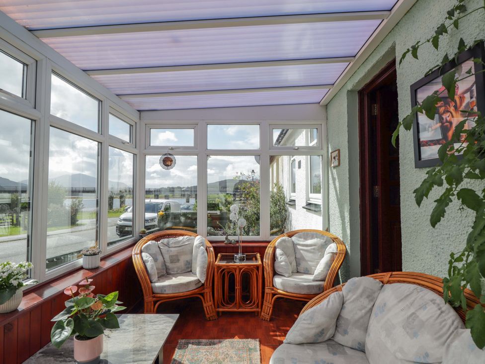 A conservatory with rattan furniture and plants at The Highlander in Dornie