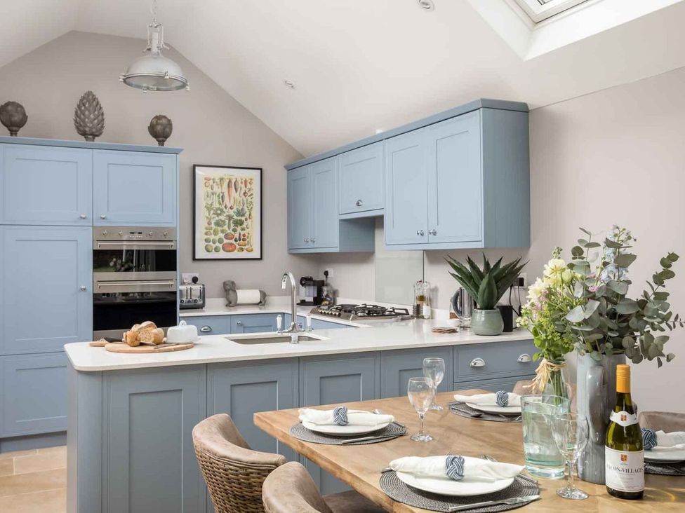 A kitchen with light blue cabinets and dining area at Lavender Cottage (Stow-on-the-Wold) Cheltenham