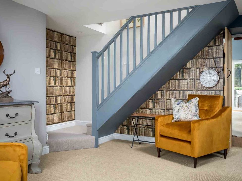 A hallway with a staircase and an armchair at Lavender Cottage (Stow-on-the-Wold) Cheltenham