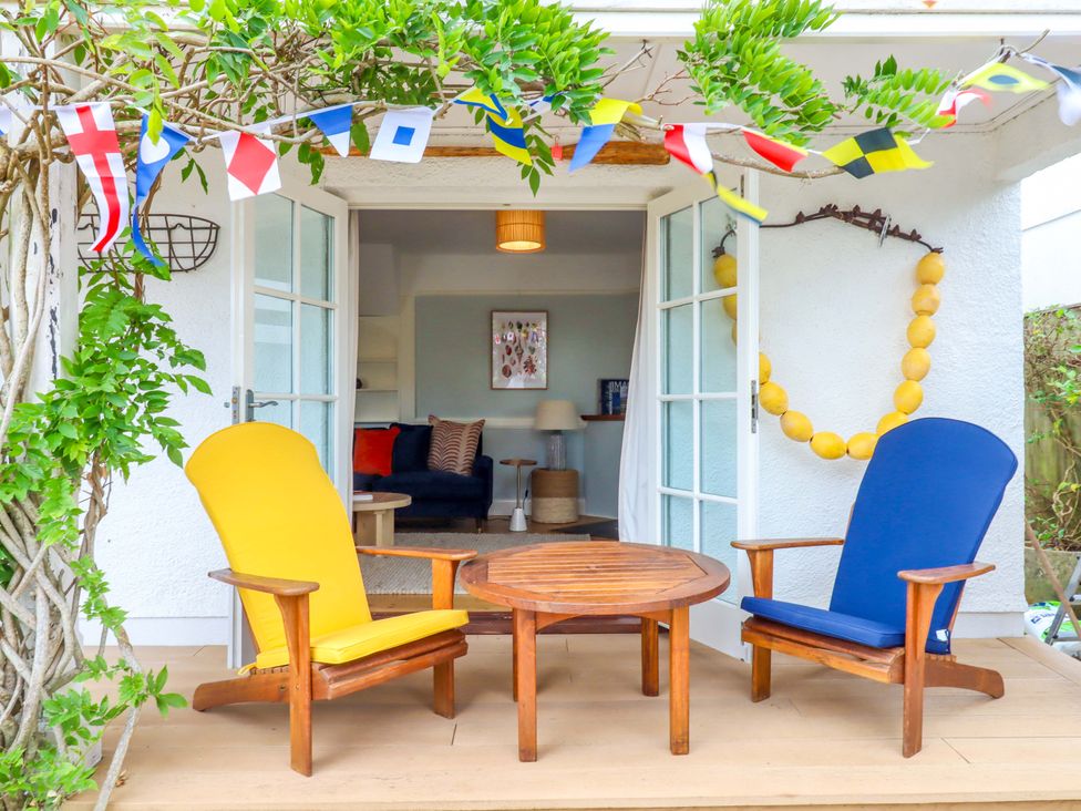 A patio with yellow and blue chairs and a wooden table at The Porthole in Newton Ferrers