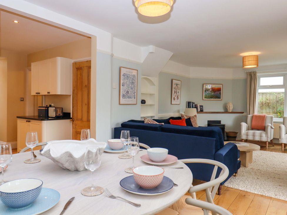 A dining area with a kitchen visible and a sofa in the background at The Porthole in Newton Ferrers