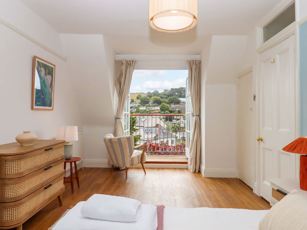 A bedroom with a window and side table at The Porthole in Newton Ferrers