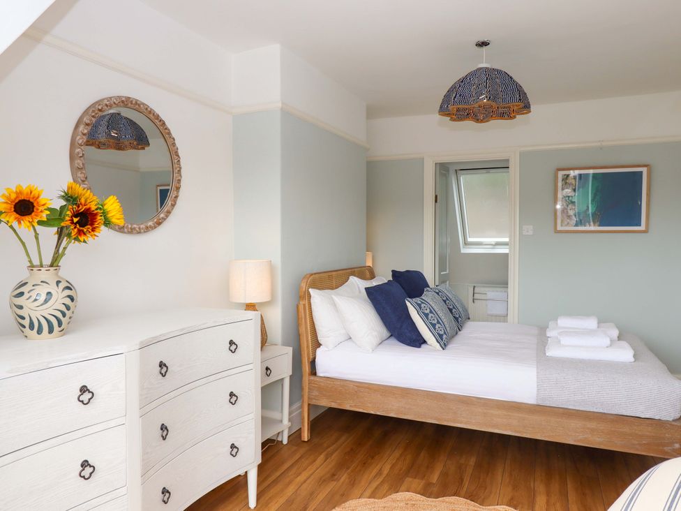 A bedroom with a bed and flowers on a dresser at The Porthole in Newton Ferrers