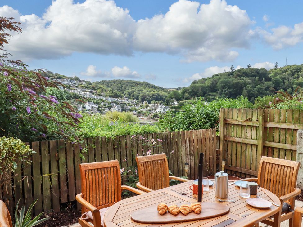 A garden with a wooden table and chairs overlooking a view at The Porthole in Newton Ferrers