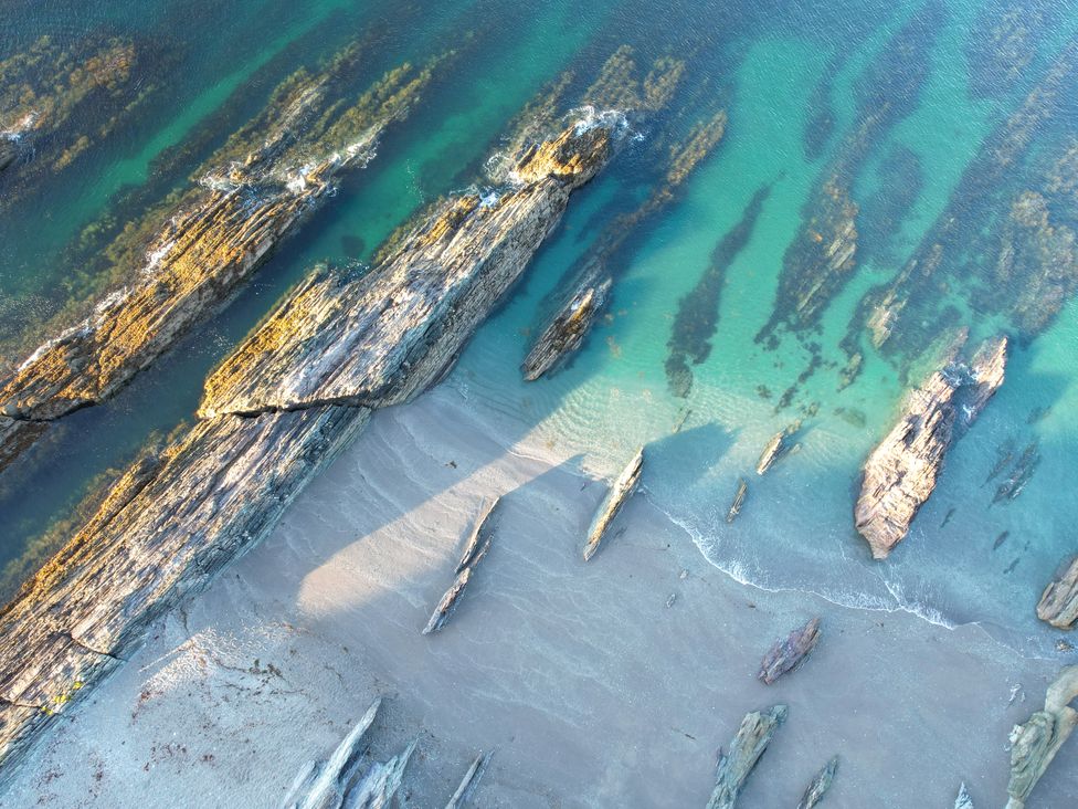 An aerial view of a beach with rocks and clear water at The Porthole in Newton Ferrers