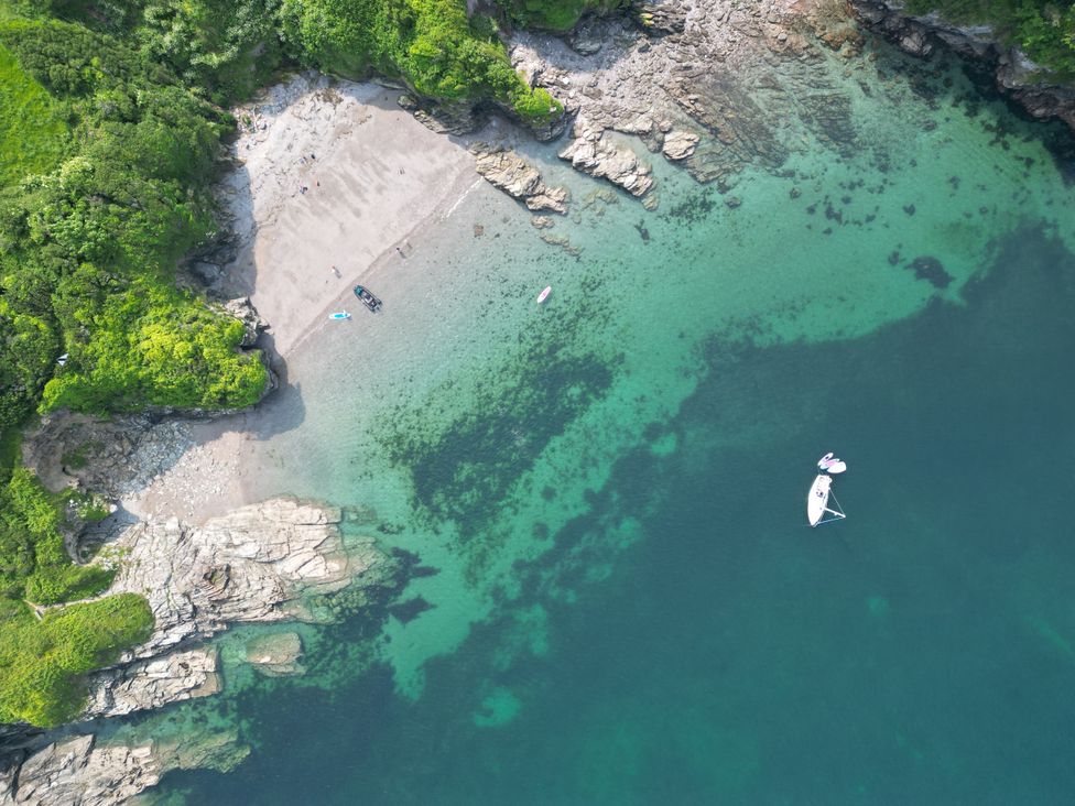 An aerial view of a beach with boats and rocky shoreline at The Porthole in Newton Ferrers