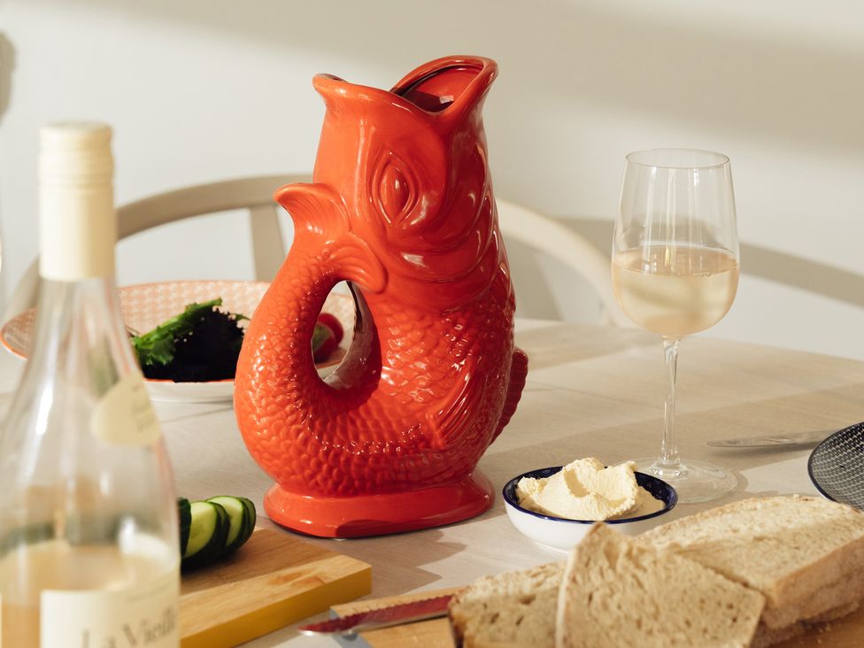 A dining table with a red fish-shaped carafe and a glass of wine at The Porthole in Newton Ferrers