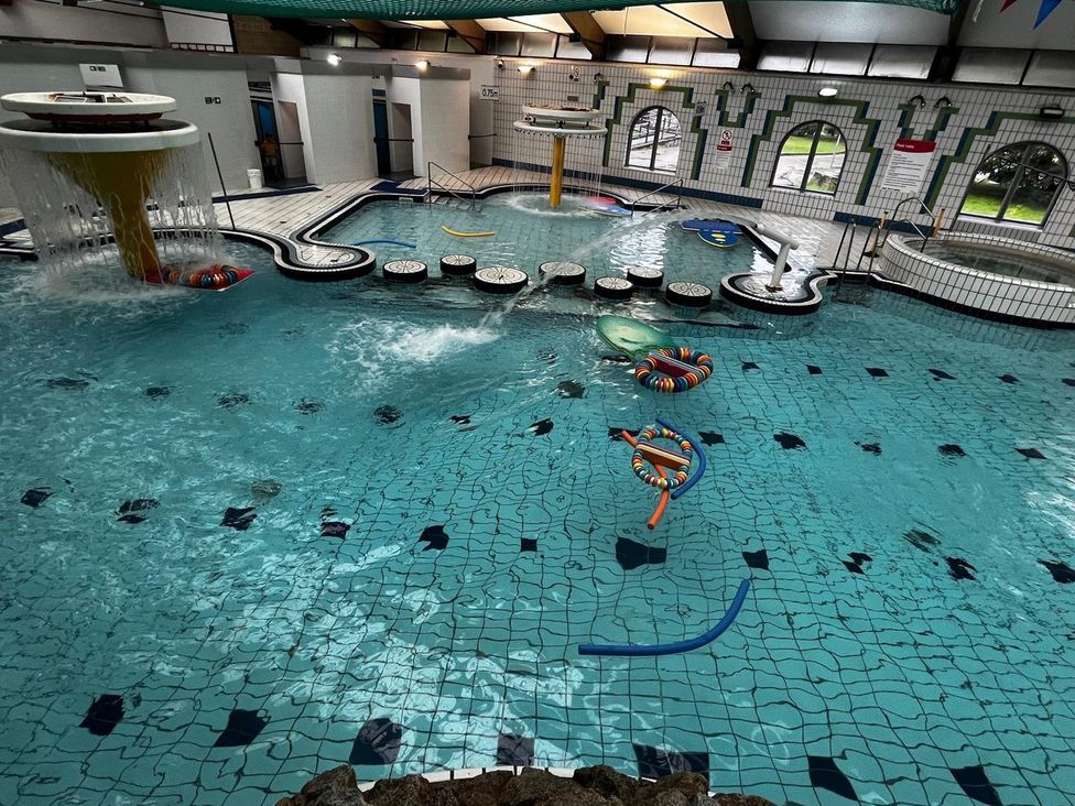 An indoor pool with a water slide and seating areas at Manorcombe 21 Honicombe Holiday Village near Gunnislake