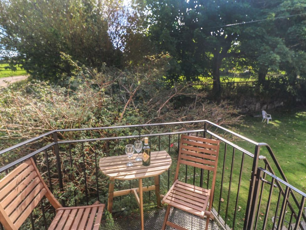 A balcony with a table and chairs overlooking a lawn at Mill House Barn