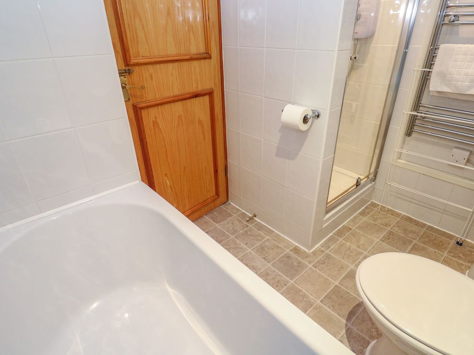 A bathroom with bathtub, shower, toilet, and wooden door at Mill House Barn, Gulval near Penzance