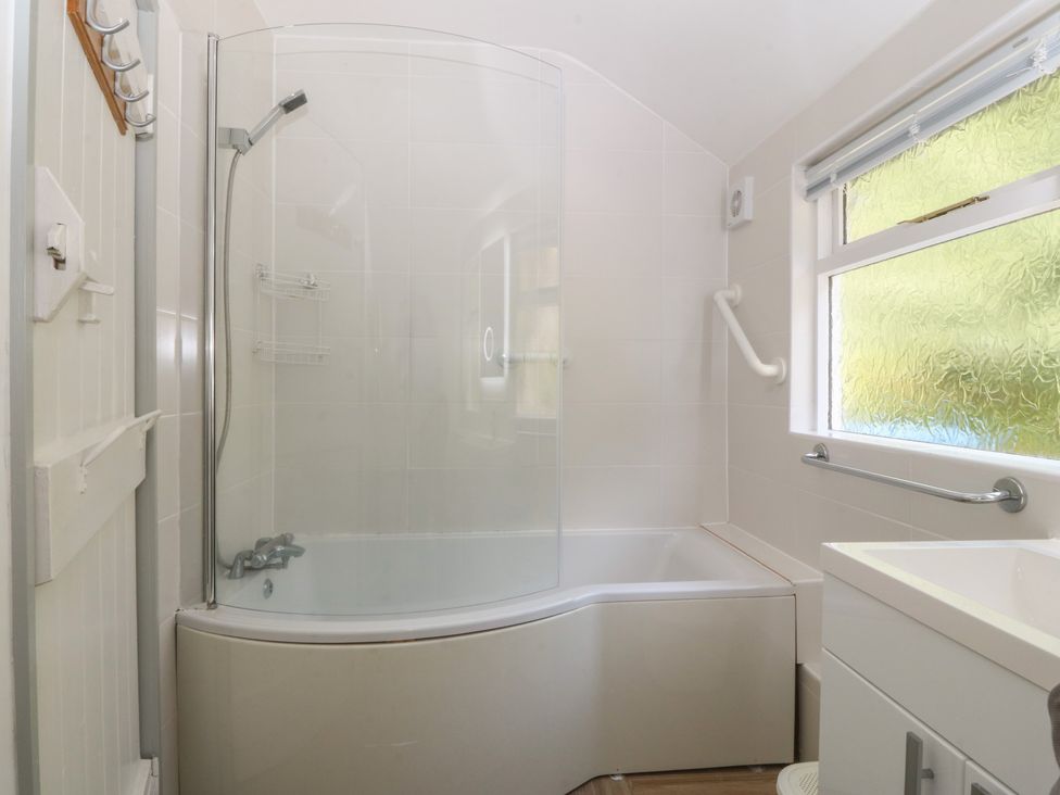 A bathroom featuring a bath tub with shower and sink at Seaview Hafod Y Graig in Morfa Bychan