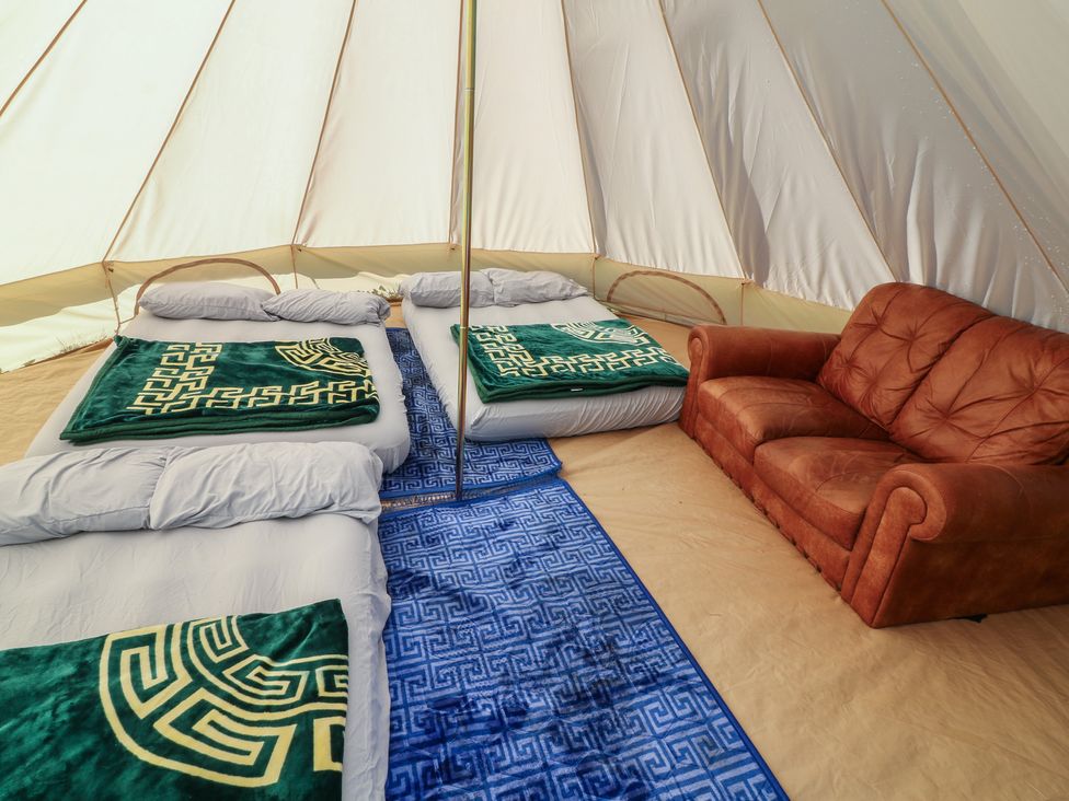 A tent interior with mattresses, pillows, blankets, and a sofa at Bell Tent Three