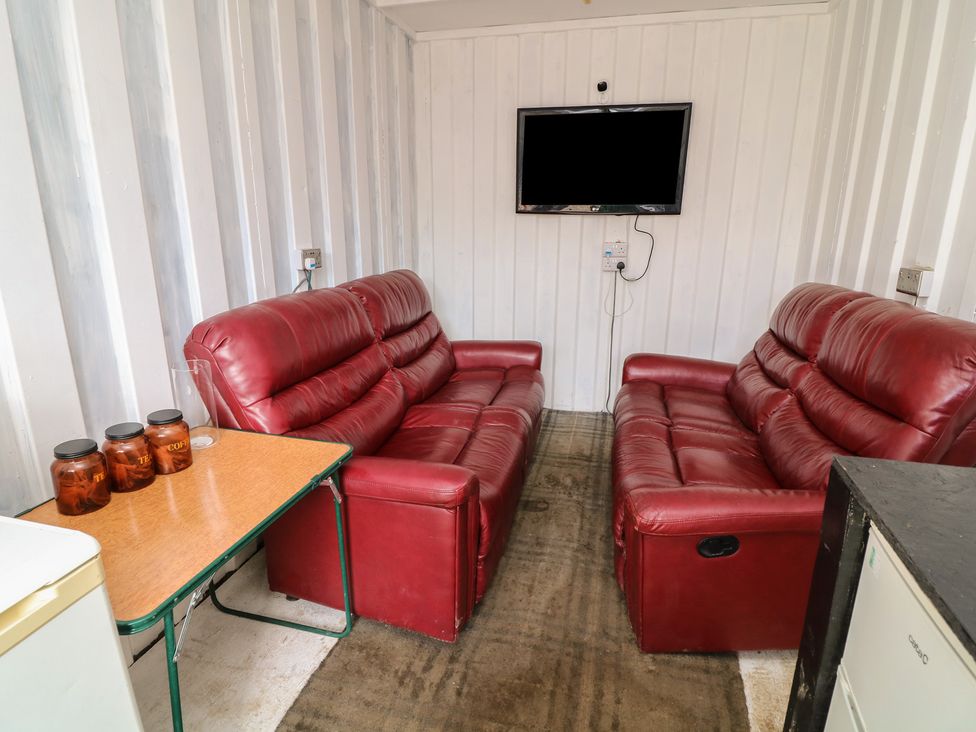 A snug area with two red sofas and a TV at Bell Tent Three