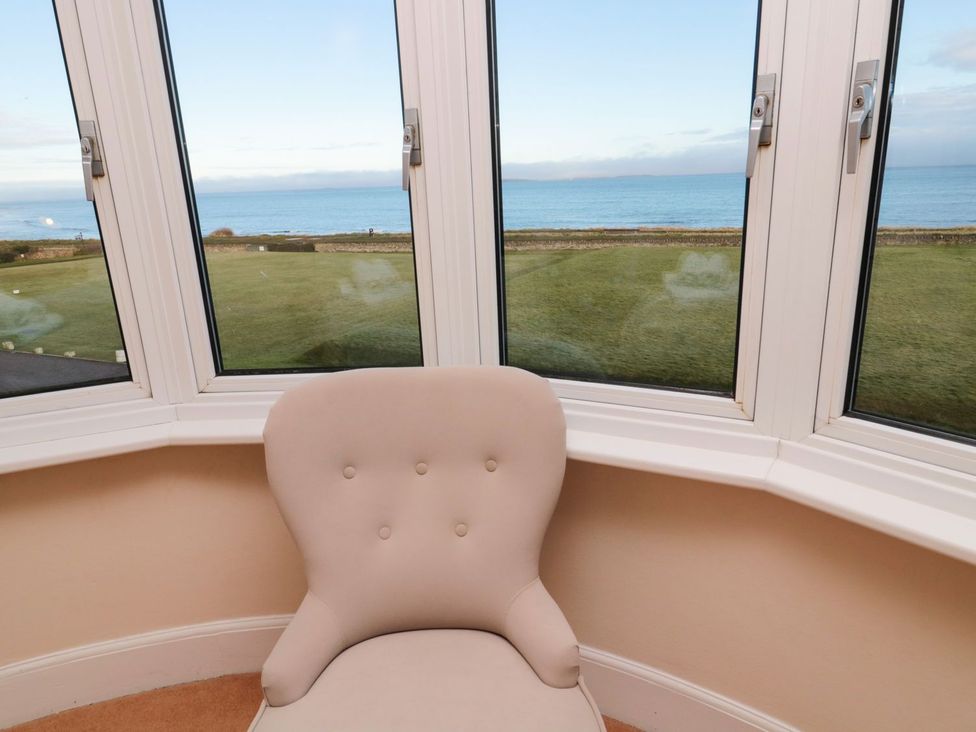 A snug room with a chair and bay windows overlooking the sea at Glen Avon in Seahouses