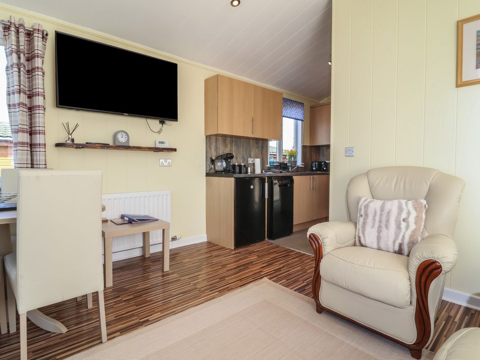 A living room with a television, chair, and kitchen area at Cody Cottage Lodge, Mullacott Park near Ilfracombe