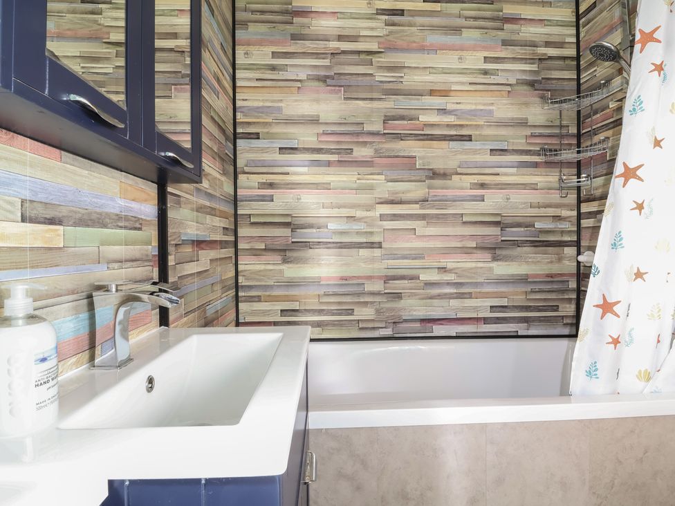 A bathroom with a sink, mirror, and bathtub at Cody Cottage Lodge, Mullacott Park near Ilfracombe