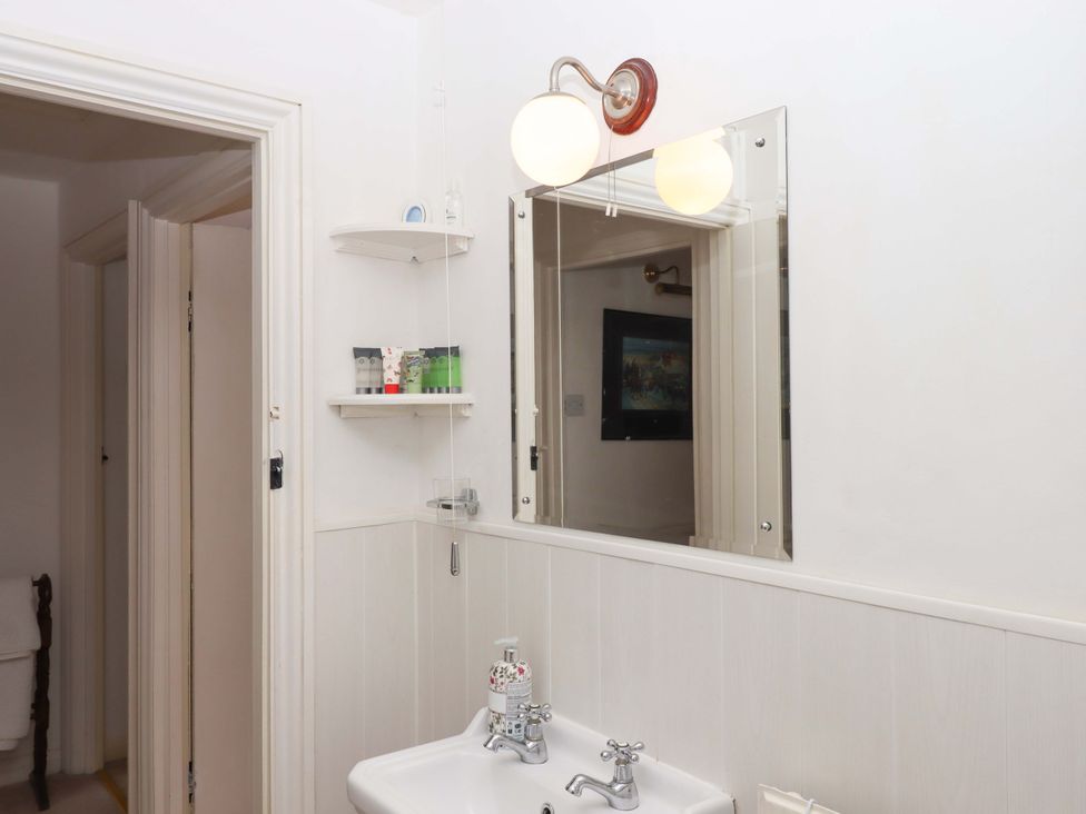 A bathroom with a sink, mirror and light at Cosy Nook in South Molton