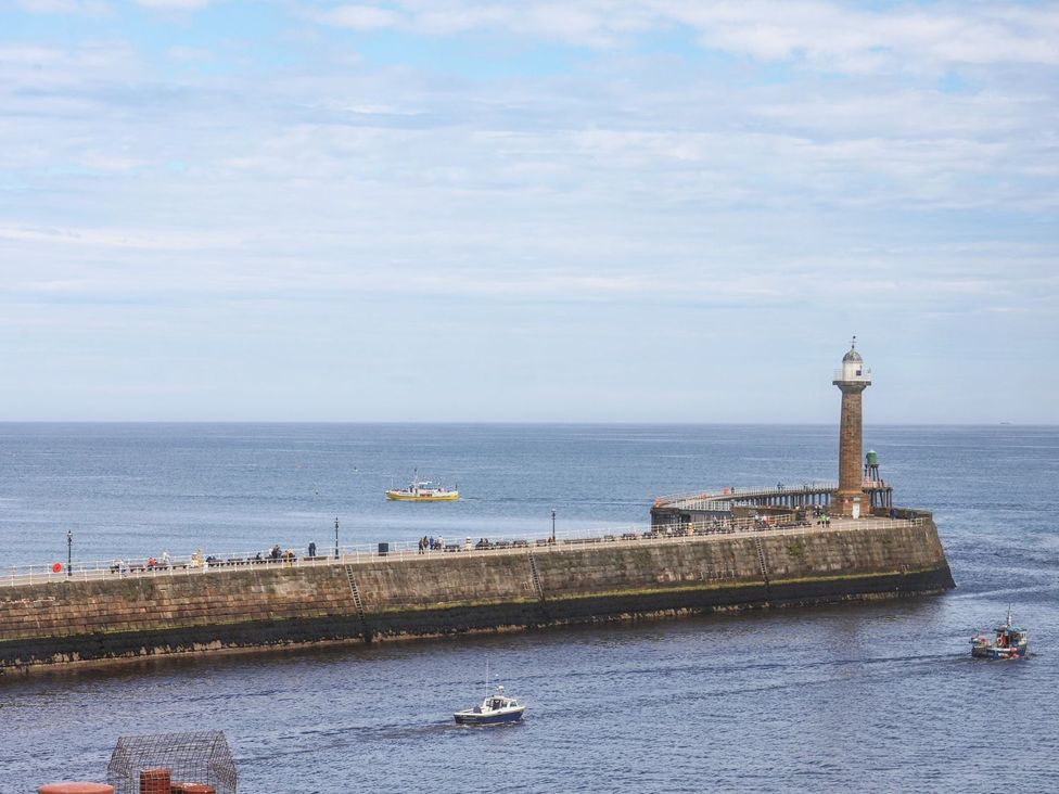 A pier with a lighthouse and boats on the ocean at Greenfingers in Whitby