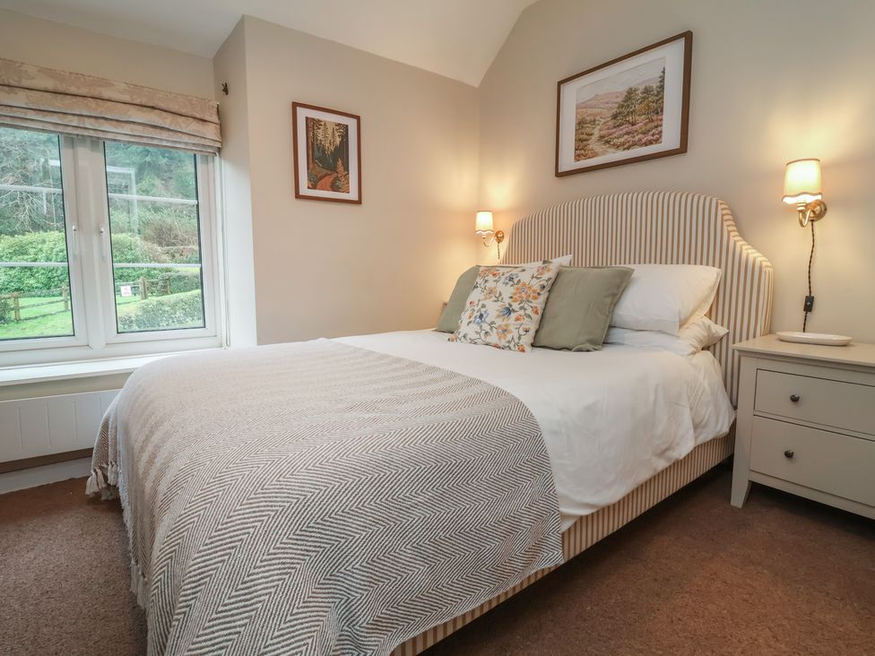 A bedroom with a bed, bedside table and window at Woodedge in Porlock