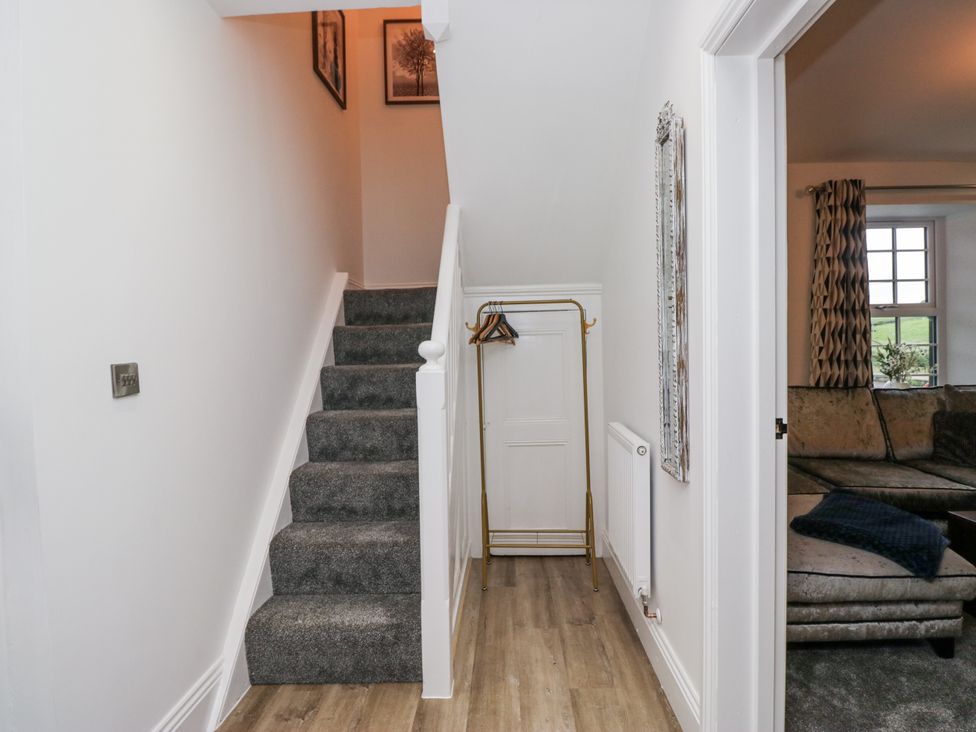 A hallway with a staircase and coat hanger at Holy Trinity Cottage in Millom