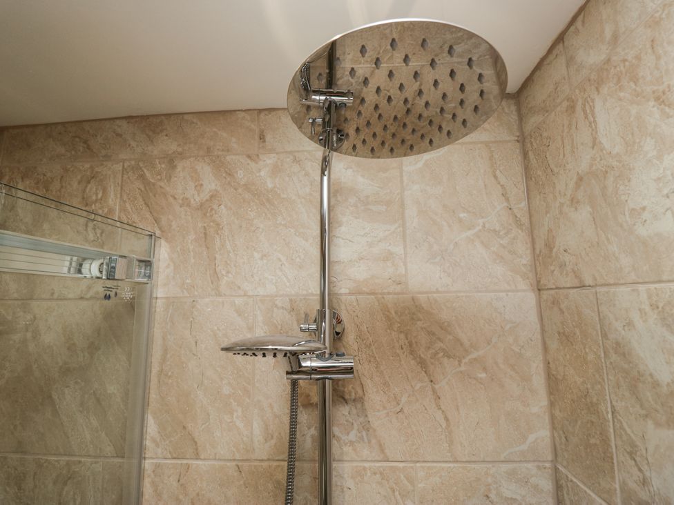 A shower with a large shower head and tile wall at Holy Trinity Cottage in Millom