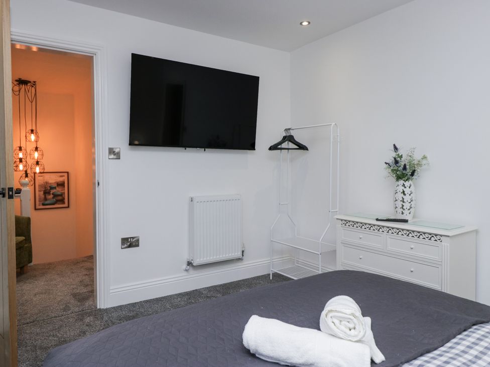 A bedroom with a bed, TV, towel, and chest of drawers at Holy Trinity Cottage in Millom