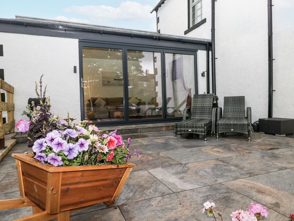 A garden patio with a flower planter and chairs at Holy Trinity Cottage in Millom