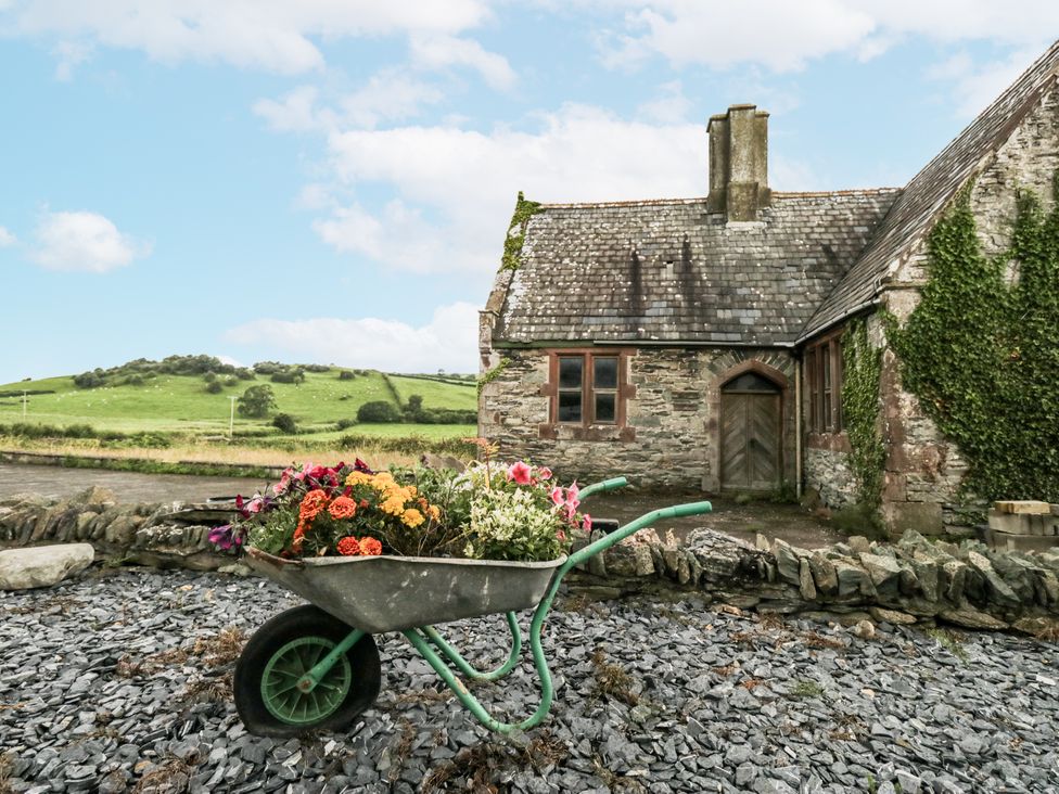 A wheelbarrow with flowers in front of a stone building at Holy Trinity Cottage in Millom