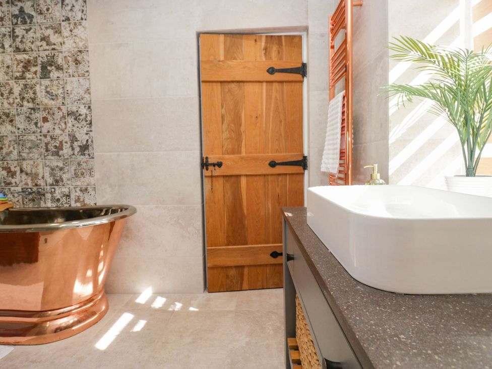 A bathroom with a copper bathtub and a white sink at Barn Howe in Lyth near Levens