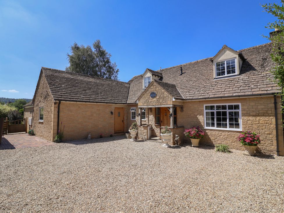 A house with a gravel driveway and flower pots at Leafield Cottage in Brockworth