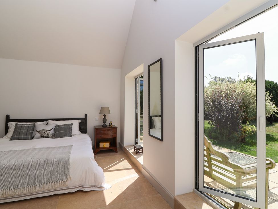 A bedroom with a bed and a window overlooking a garden at Leafield Cottage in Brockworth