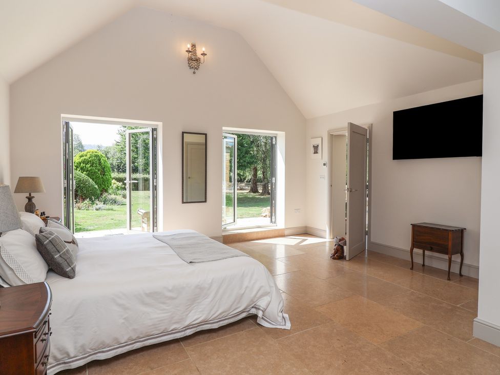 A bedroom with a bed and windows at Leafield Cottage in Brockworth