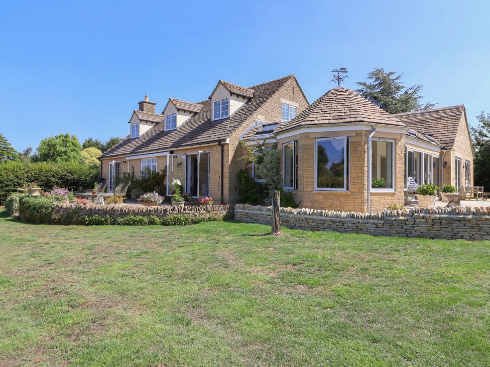 A house with stone walls and a lawn at Leafield Cottage in Brockworth