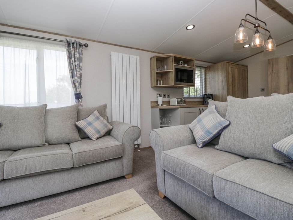 A living room with sofas and a kitchen area at Grasmoor View Lodge