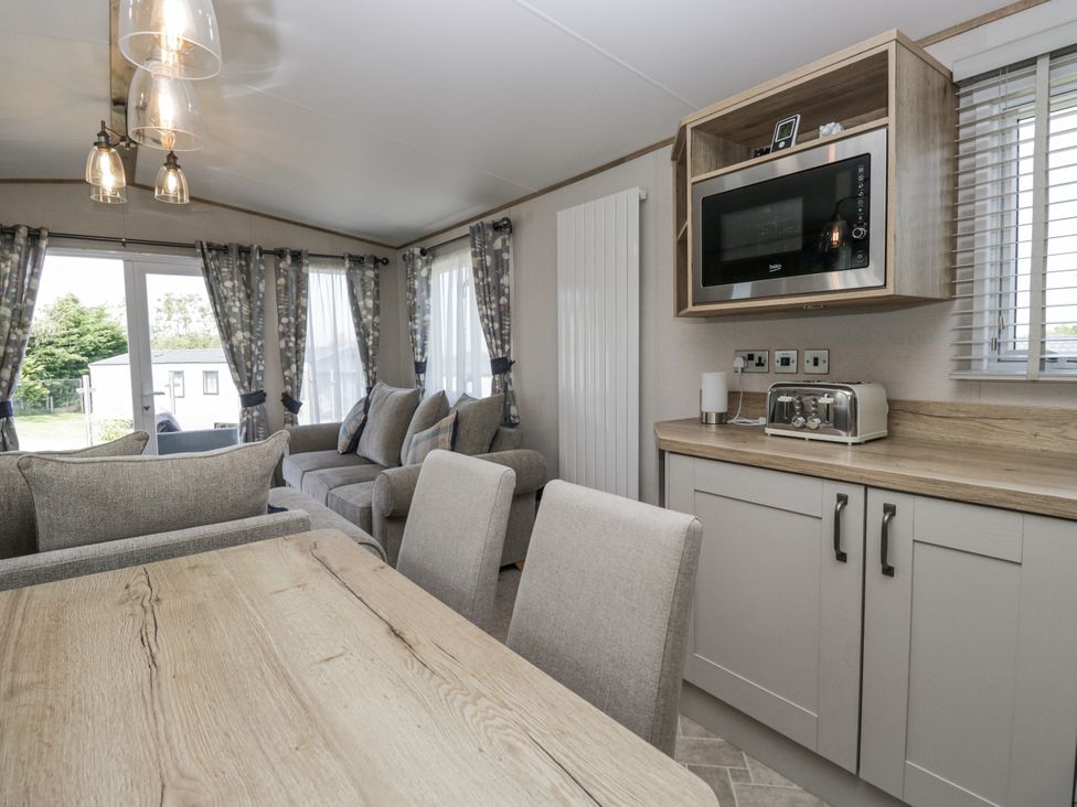 A living room with a dining area and kitchen appliances at Grasmoor View Lodge