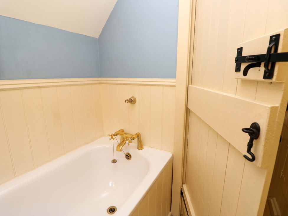 A bathroom with a bathtub and a door at Smugglers Cottage in New Milton