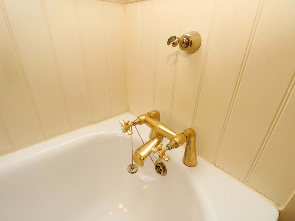A bathtub with a gold faucet and bath tap at Smugglers Cottage in New Milton