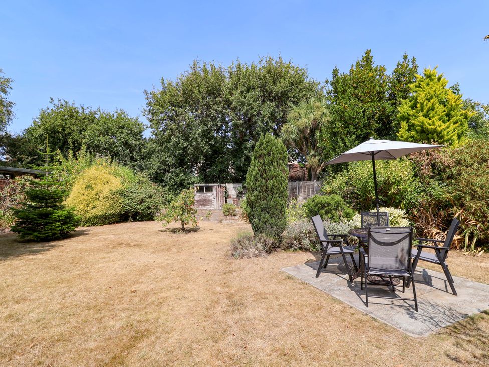 A garden with a table and chairs under an umbrella at Smugglers Cottage in Barton On Sea