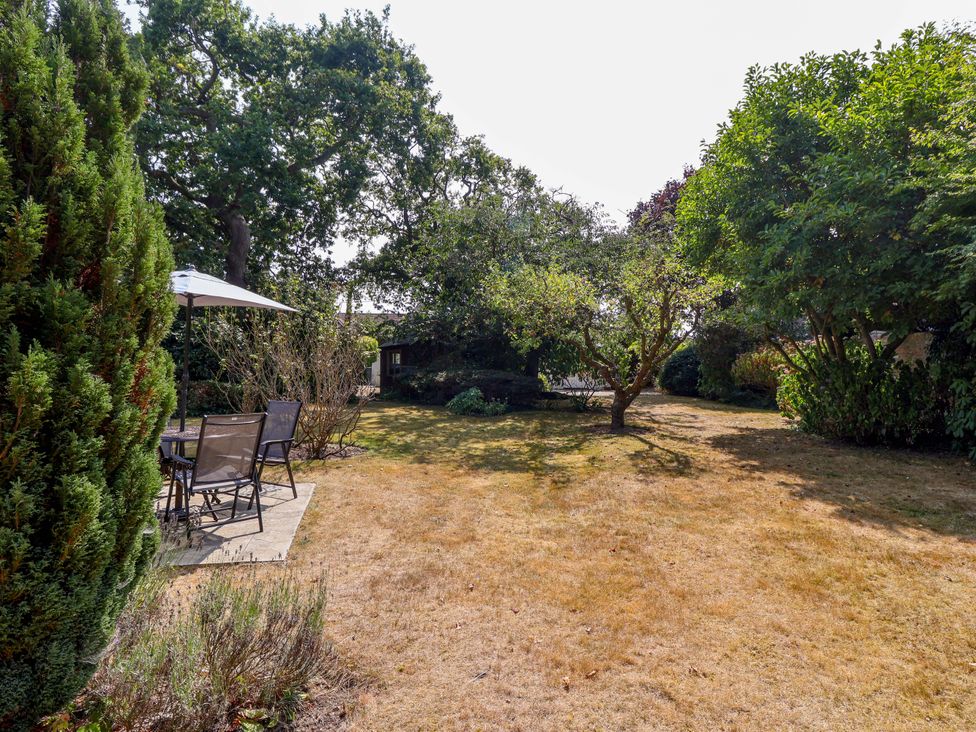 A garden with grass, trees, table and chairs at Smugglers Cottage in Barton On Sea