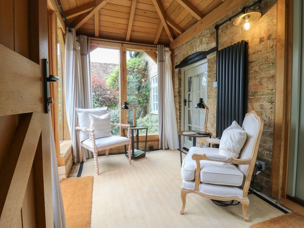A conservatory with an armchair and small table at Little Barn @ Orwell