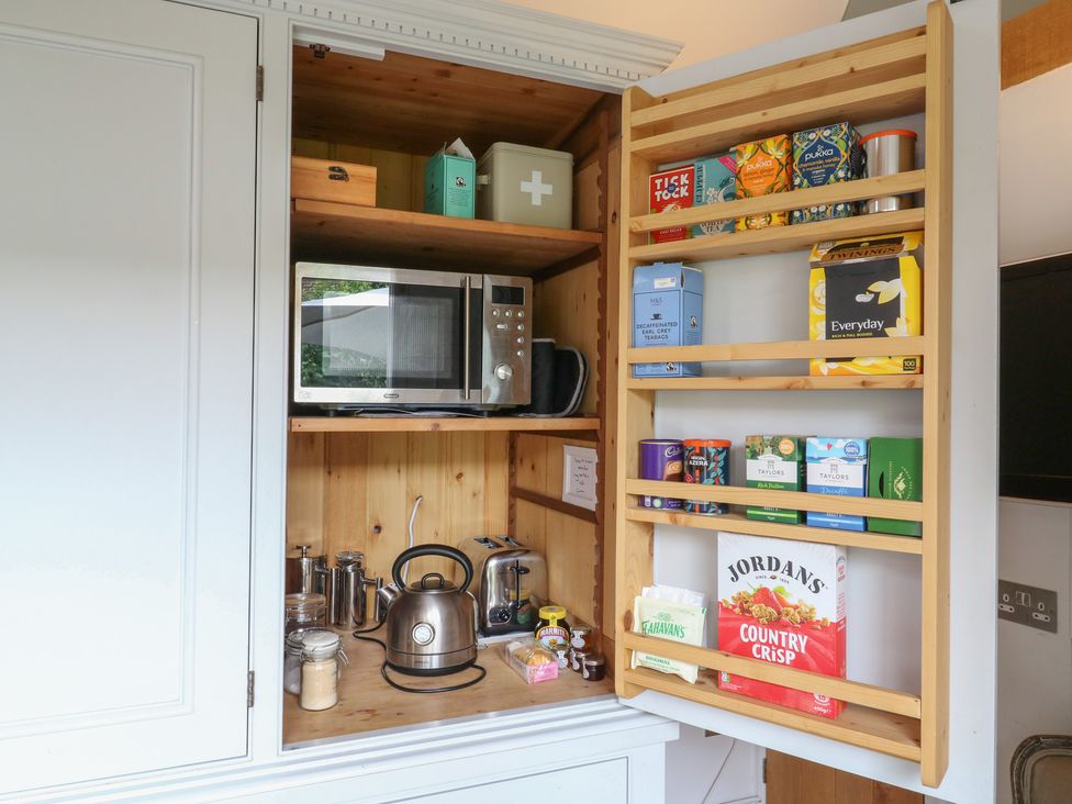 A kitchen cabinet with a microwave, kettle, tea bags, and jars at Little Barn @ Orwell