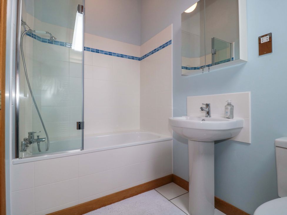 A bathroom with a bathtub, sink, and wall-mounted mirror at Stowey Mead Stables Bishop Sutton