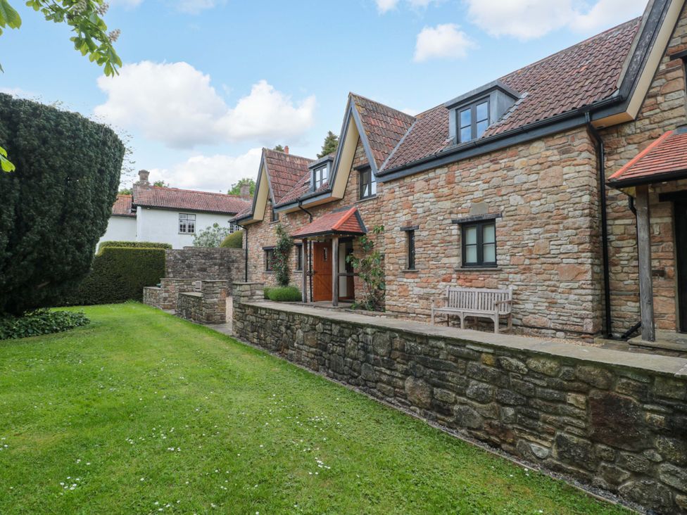 A garden with a stone wall and benches at Stowey Mead Stables in Bishop Sutton
