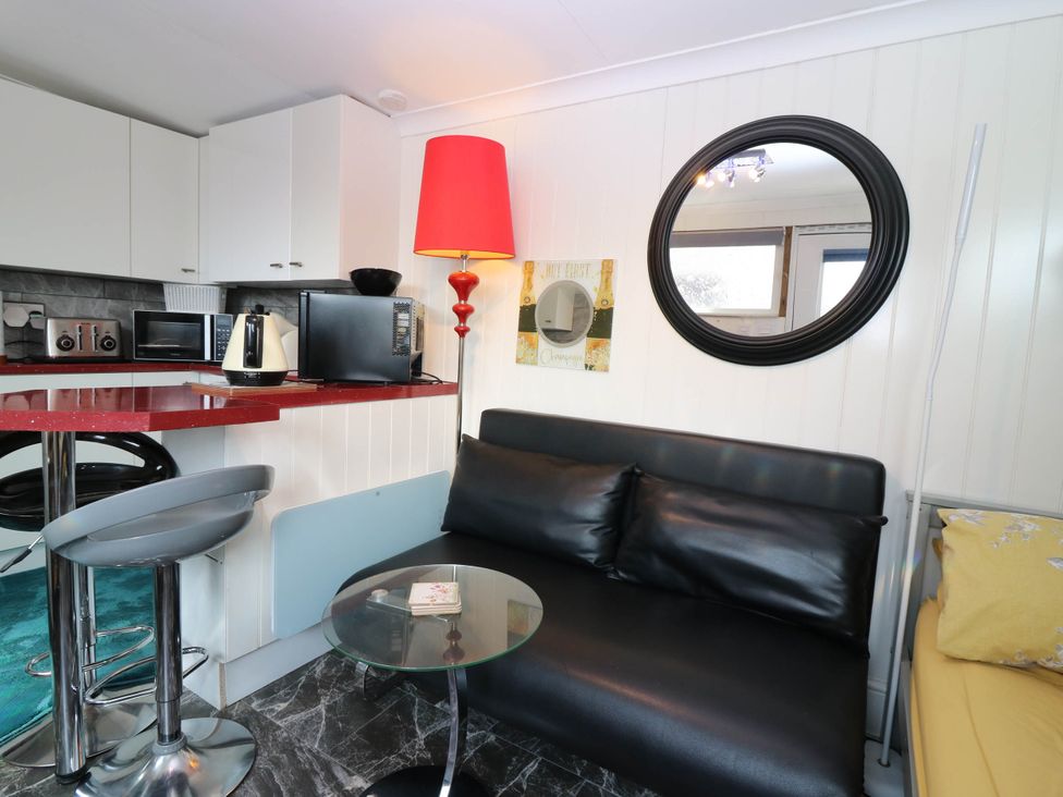 A living room with a sofa, coffee table, and kitchenette at The Cabin in East Wemyss near Buckhaven
