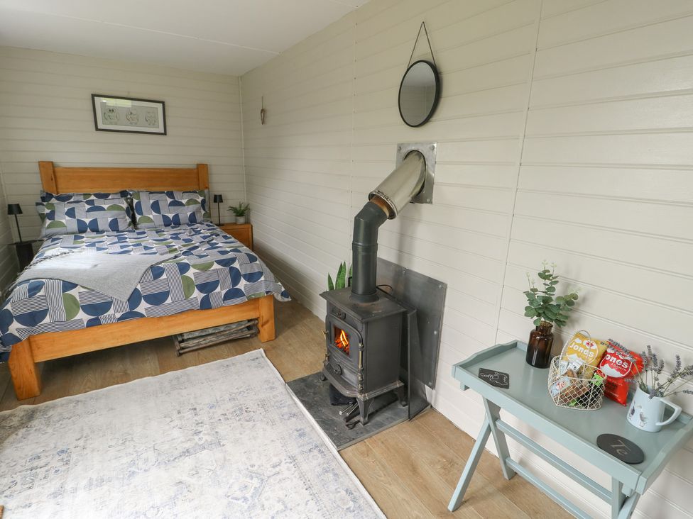 A bedroom with a bed, stove and table at Seiriol Shepherds hut Ty Croes