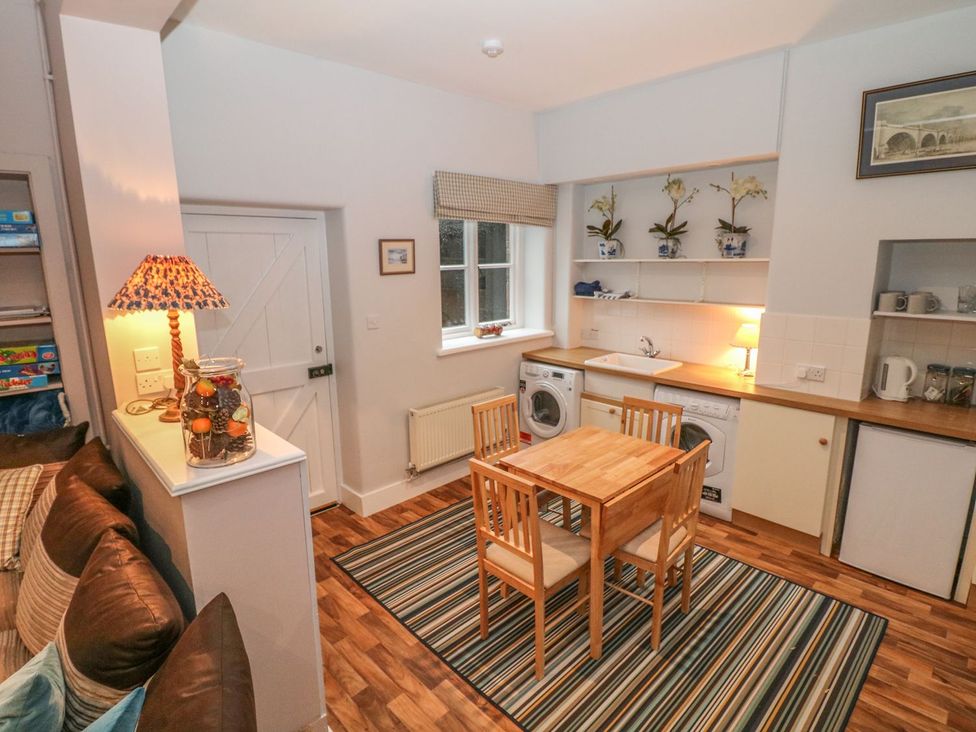 A kitchen with a table and chairs along with a washing machine at The Bothy in Wildboarclough
