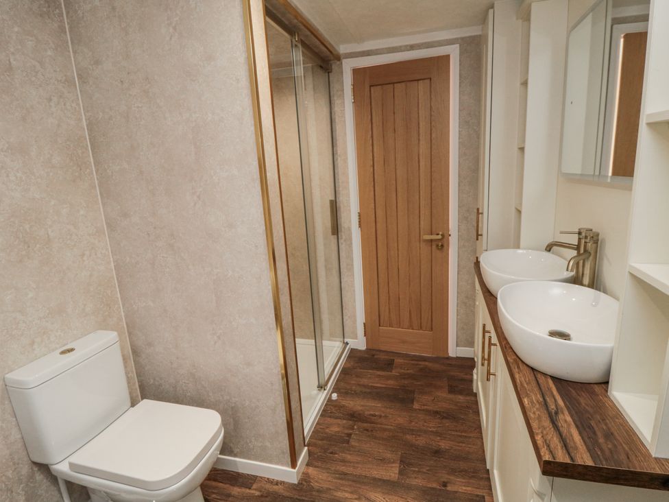 A bathroom with a toilet, shower, sinks, and storage space at The Cabin in Thornton Dale