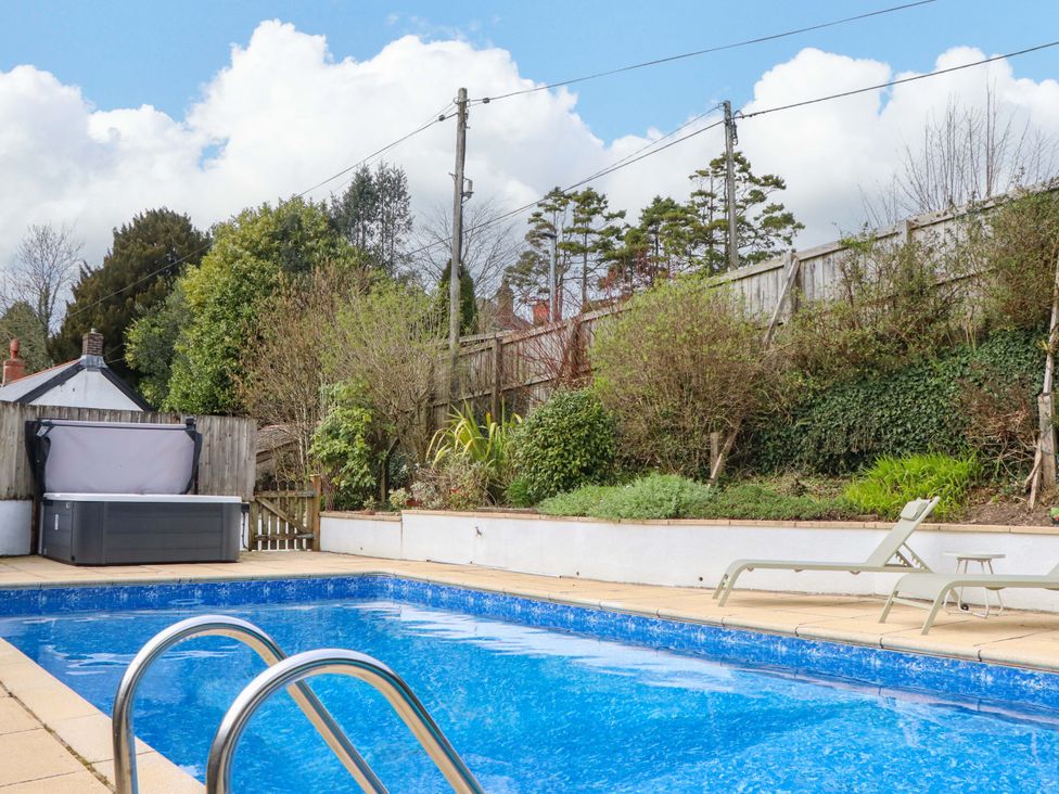 A swimming pool with deck chairs and a hot tub at Town Farm Cottage in Barnstaple